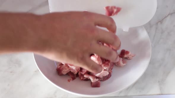 Closeup of a males hand pouring in the chopped pork into the bowl. Home cooking concept. alt