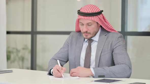 Middle Aged Arab Businessman Writing on Paper in Office alt