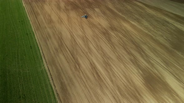 Spring agricultural land. Tractor with a cultivator on a spring field. Aerial photography. alt