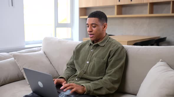 Optimistic Man in Casual Wear Using Laptop While Sitting on the Couch