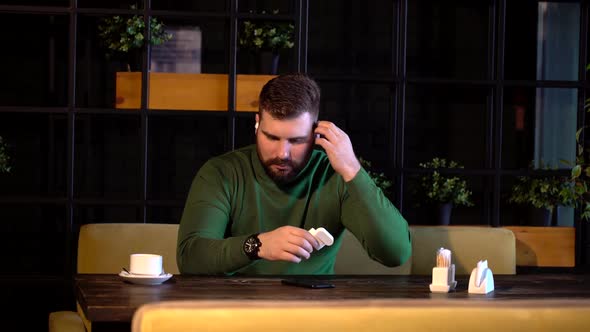a Hipster Man Sits in a Cafe and Listens To Music in Bluetooth Headphones