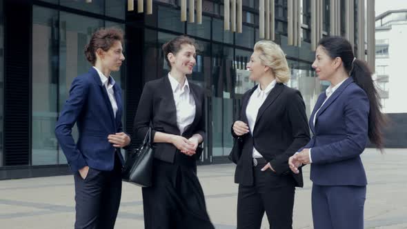 Female Business People in Suits Stand and Discuss Business, Looking at Camera. They're All Working