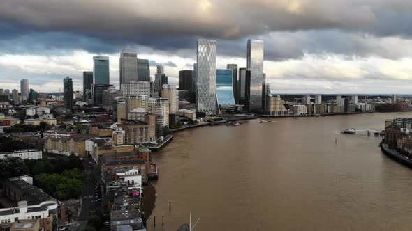 Reverse aerial view of storm dark clouds over Canary Wharf skyscrapers at sunset alt