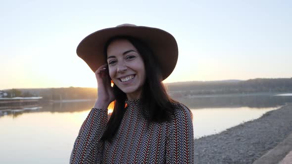 Young Girl with Hat Smiling Posing at Camera Near the Lake alt