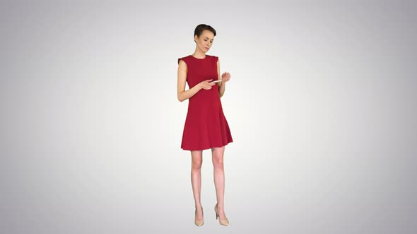 Young Happy Attractive Female in Red Dress Texting on the Phone on Gradient Background. alt