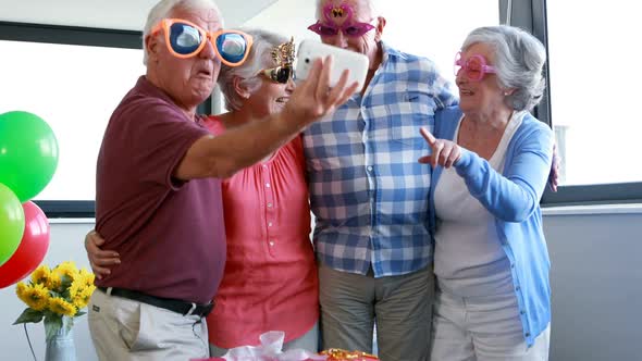 Senior citizens taking selfie on mobile phone during birthday party alt