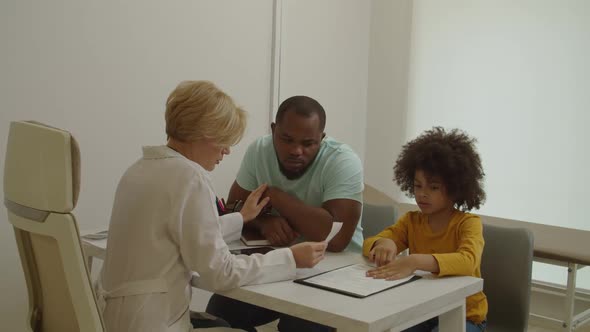 Empathetic Woman Doctor Telling Bad News to Upset Black Father About Illness of Little Son at Clinic alt