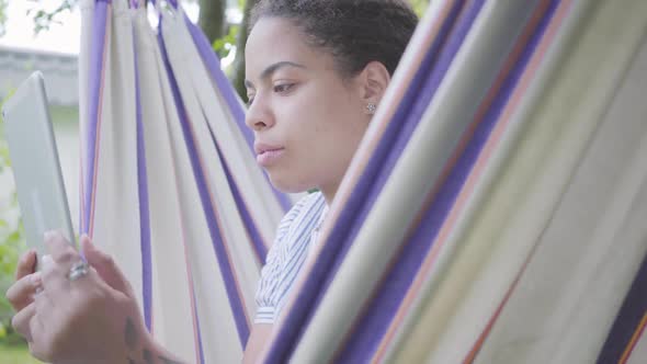 Face of Young African American Woman Sitting in the Hammock, Relaxing in the Garden alt