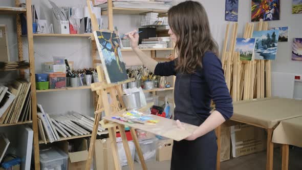 Student Artist Girl Is Holding Palette with Paints and Standing Near Easel alt