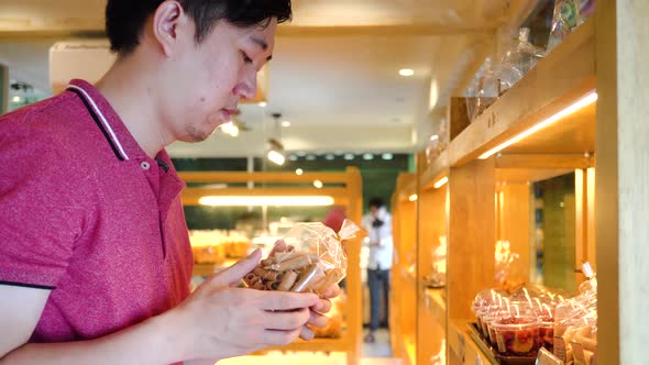 Mid Shot of Asian Young Man Shopping and Consider Buying Stuff in Retail Grocery Store alt