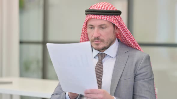 Middle Aged Arab Businessman Reading Reports while Sitting in Office alt
