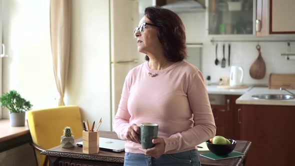 Serious Thoughtful Old Woman Looking Away in Sad Thought Drink Tea in Kitchen alt