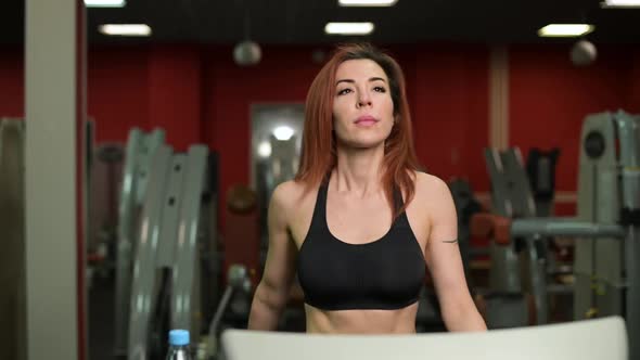 Young woman warming up and doing stretching while walking on a treadmill alt
