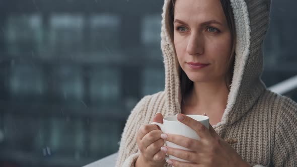 Woman Stays on Balcony During Snowfall with Cup of Hot Coffee or Tea alt