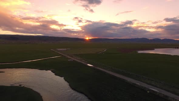 Aerial view flying backwards over winding river during colorful sunset alt