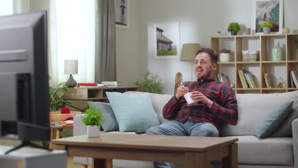 Young Handsome Man Lunchs Chinese Noodle From Delivery and Watching Tv at Home in the Living Room alt