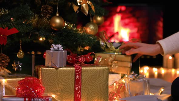 Woman Placing Gifts under Christmas Tree near Fireplace
