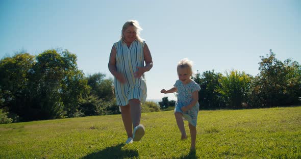 Middle Aged Woman Dancing with Her Granddaughter on Grass at Sunny Summer Day alt