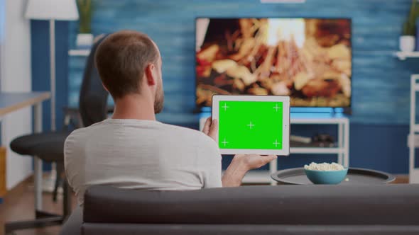 Back View of Man Holding Digital Tablet with Green Screen Watching Social Media Video Content alt