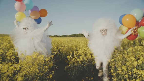 Two Funny Clowns Mime in White Air Suits and with Colored Balloons Walk Around the Field