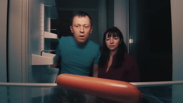 Hungry Man and Woman Open the Refrigerator at Night and Take a Sausage Night Zombie