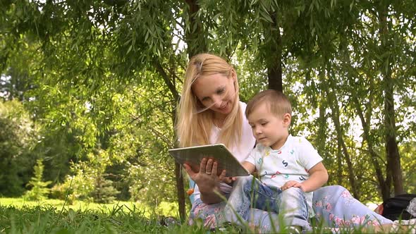 Happy Mother and Her Little Son Enjoying Playing on Tablet Computer in the Park. Slow Motion. alt