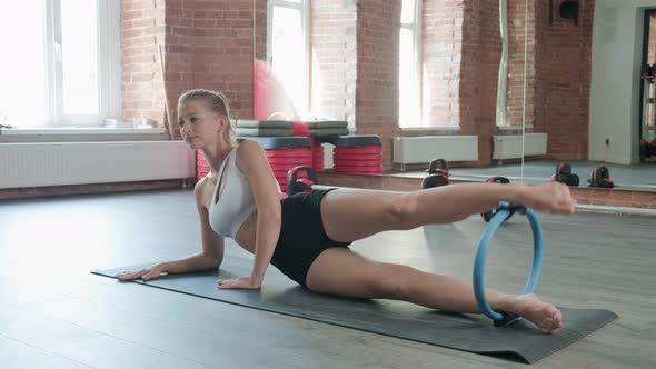 Athletic Girl Squeezes Pilates Ring with Legs at Gym