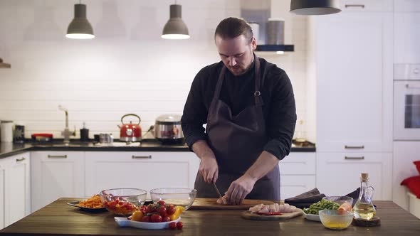 Young Cute Chef Cuts Chicken Meat on a Wooden Board at the Home Kitchen alt