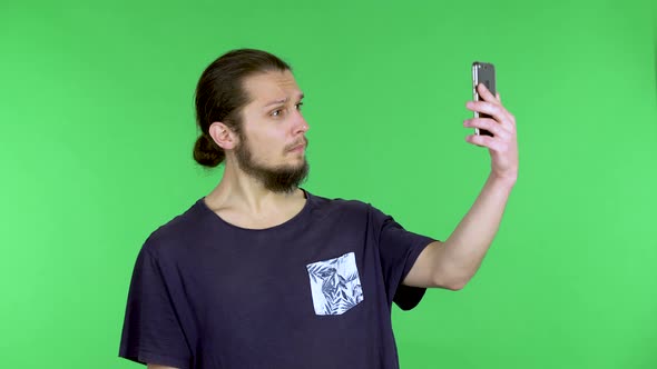 A Man Takes a Selfie on His Smartphone Smiles at the Camera and Makes a Victory Gesture Then Looks alt
