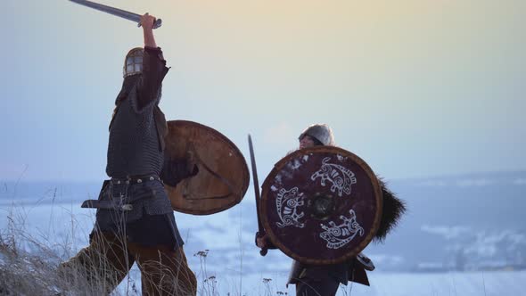 Two viking are fighting with axes and shields on the winter meadow. alt