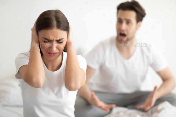 Unhappy Woman Covering Ears While Angry Husband Shouting In Bedroom