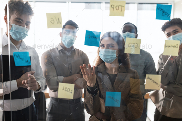 Businesspeople having meeting using sticky post-it notes on glass wall