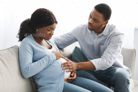 Pregnant woman having labor pains, sitting with husband on couch