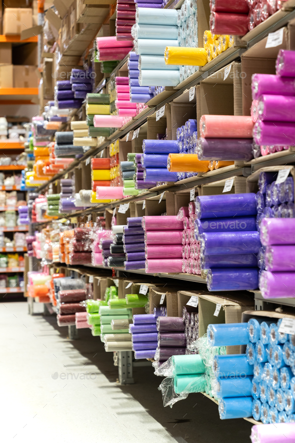 Fabric store with rolls of textile on shelves. Assortment of colorful clothes for sale in warehouse