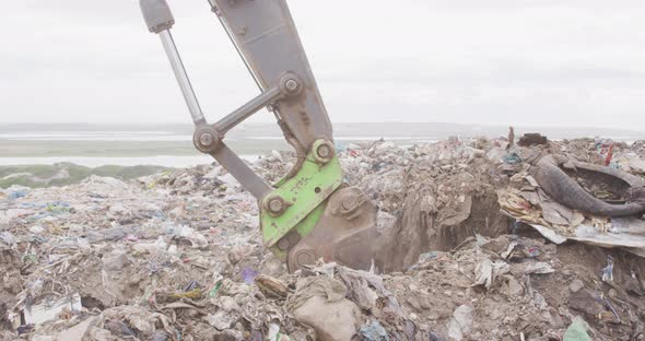 Digger clearing rubbish piled on a landfill full of trash alt