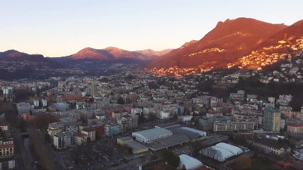 Aerial view of a beautiful city surrounded by mountains, next to a lake, during a sunset in autumn. alt