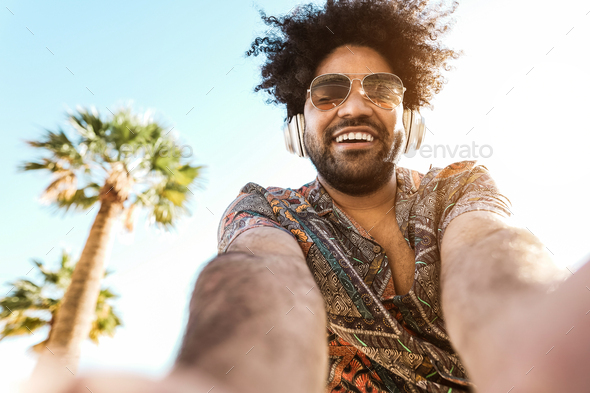 African american man listening music with headphones outdoor with palm trees in background - Stock Photo - Images