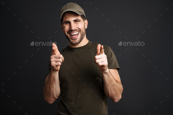 Joyful masculine military man smiling and pointing fingers at camera
