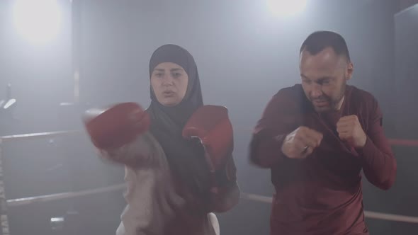 Focused Muslim Woman Punching Air As Trainer Endorsing Female Boxer on Boxing Ring. Portrait of alt