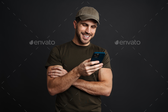 Happy masculine military man smiling and using mobile phone
