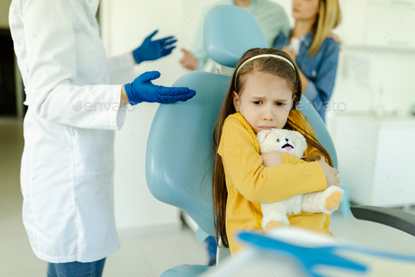 Portrait of scared girl at dentist\'s office. Dentist extracted tooth of little girl