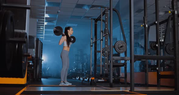 Girl in the Gym Doing Squats with a Barbell. Smoke, Darkness, Sports Hall alt