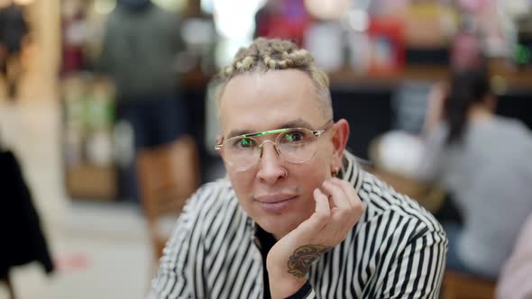 Closeup of a Beautiful Portrait of a Homosexual Man with Glasses Sitting at a Table in a Shopping alt