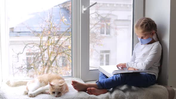 A Preschooler Girl with a Pet Is Sitting on the Windowsill