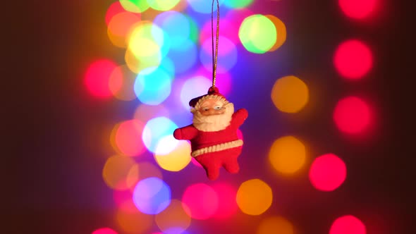 New Year Santa Claus Toy Hanging on a Background of Holiday Lights alt