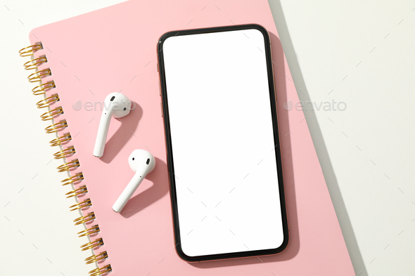 Phone with empty screen, headphones and copybook on white background, top view