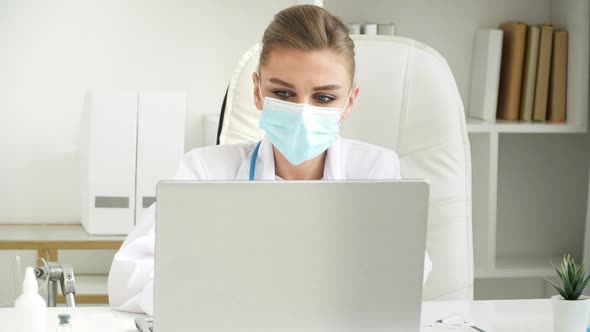 Female Doctor in Mask Works at Laptop in Clinic alt