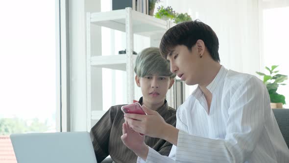 Asian gay couple using laptop and smartphone, discussing somthing seriously alt