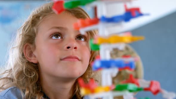 Cute Caucasian schoolgirl studying DNA model in classroom at school 4k alt