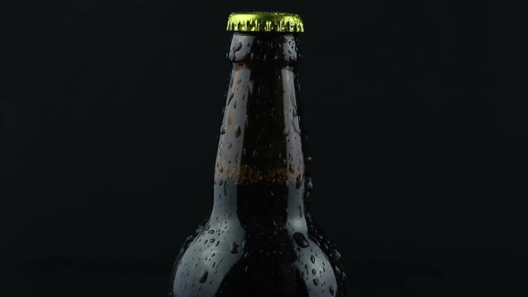 Drops of Condensate Flow Down a Beer Bottle on a Dark Background